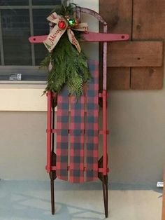 a red and black plaid christmas sled hanging from the side of a building with a wreath on it