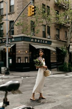 a woman is walking down the street with flowers in her hand and holding a basket