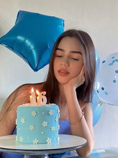 a woman sitting in front of a blue cake with lit candles on it and balloons behind her