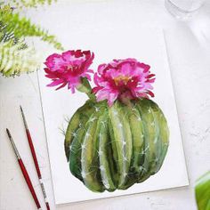 a cactus with pink flowers on it sitting next to some paintbrushes