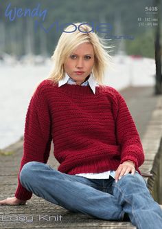 a woman sitting on a dock wearing a red sweater