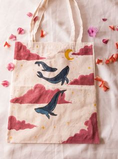 a tote bag with two dolphins in the sky on it and pink flowers scattered around