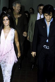 the man and woman are walking down the hall together, dressed in black suits with pink fringes