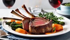 a white plate topped with meat and veggies next to two glasses of wine