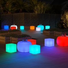 several illuminated stools and tables on a deck at night with trees in the background