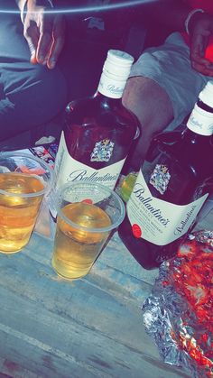 three bottles of alcohol sitting on top of a wooden table next to two glasses filled with liquid