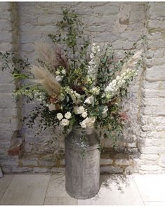 a vase filled with lots of flowers on top of a floor next to a brick wall