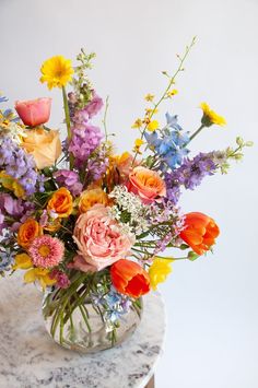 a vase filled with lots of different colored flowers on top of a marble table next to a white wall