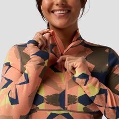 a woman in an orange and blue shirt smiles while holding her hands on her chest