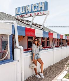 a woman leaning on the side of a building next to a sign that reads lunch lobster roll