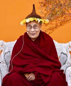 a man sitting on top of a white chair wearing a red robe and flower crown