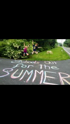 two people jumping in the air with chalk writing on the road and trees behind them