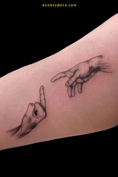 two hands touching each other with one hand pointing at the other tattoo on someone's arm