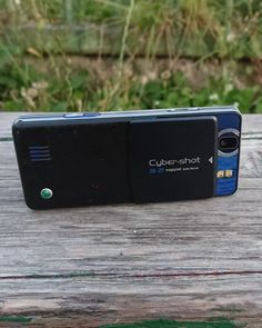 a cell phone sitting on top of a wooden table next to green grass and bushes