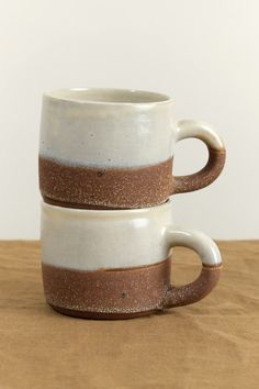 two coffee mugs stacked on top of each other with brown and white glaze