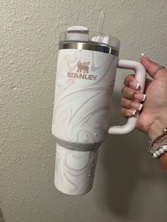 a person holding a white coffee cup in their right hand with the word stanley on it