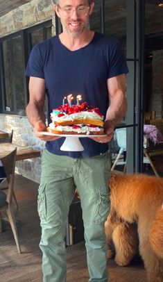 a man holding a cake on top of a wooden table next to a brown dog