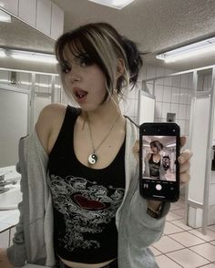 a young woman holding up a cell phone in a room with white tile flooring