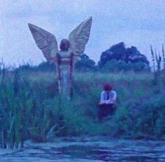 an angel statue sitting in the grass next to a body of water