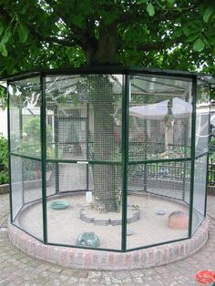 a bird cage in the middle of a brick patio with a tree and fence around it