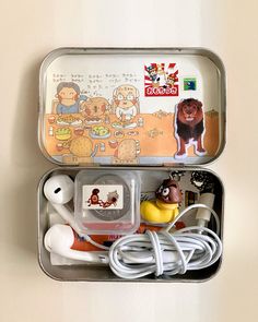 an open tin can with various items in it on a white surface, including headphones and earbuds