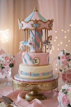 a carousel cake with pink, blue and gold icing sits on top of a table