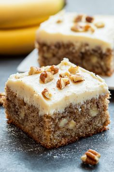 two pieces of cake with white frosting and nuts sitting on a table next to bananas