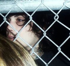 a woman behind a chain link fence looking at the camera with her face through the bars