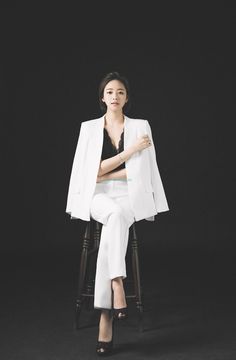 a woman sitting on top of a wooden chair wearing a white suit and black heels