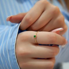 a close up of a person wearing a gold ring with a green stone on it