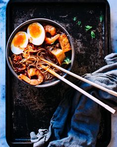 a pan filled with noodles and eggs next to chopsticks on top of a table