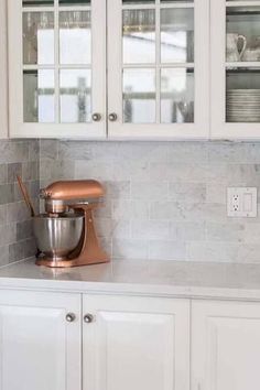 a kitchen with white cabinets and marble counter tops, including a mixer on the counter