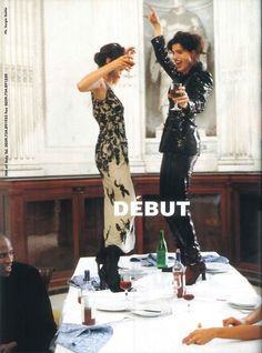 two women dressed in black and white dancing at a table with wine glasses on it