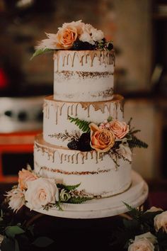 a three tiered cake with flowers and greenery on the top is sitting on a table