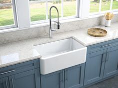 a kitchen with blue cabinets and white marble counter tops, an island sink and large windows