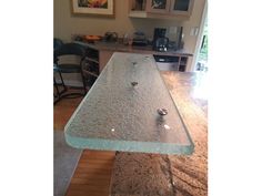 a glass table top in the middle of a kitchen with chairs and cabinets behind it