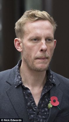 a man with a flower on his lapel looks at the camera while standing in front of a building