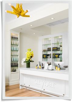 a white counter with yellow flowers and bottles on the shelves behind it in a salon