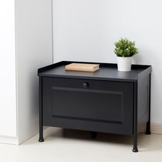 a small black table with a book on top and a plant in the corner next to it