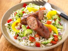 a plate filled with rice, meat and veggies next to a fork on a wooden table