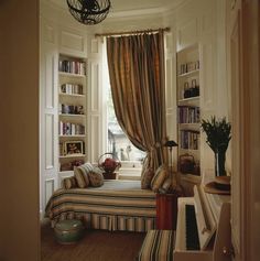 a living room filled with furniture and bookshelves next to a window covered in curtains