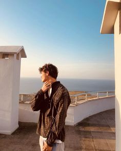 a man standing on top of a roof next to a white building and looking at the ocean