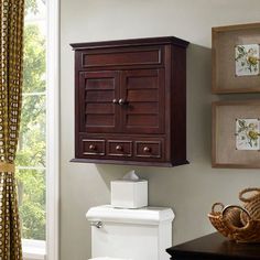 a wooden cabinet above a toilet in a room with curtains and pictures on the wall