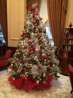 a decorated christmas tree in the middle of a room with red and silver decorations on it