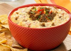 a red bowl filled with white cheesy dip surrounded by tortilla chips