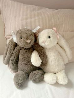 two stuffed animals sitting next to each other on a bed