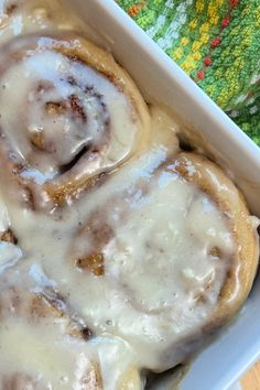 cinnamon rolls with icing in a white casserole dish on a colorful towel