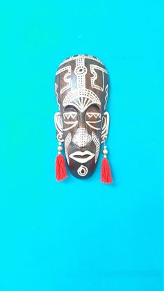 an african mask with red tassels on it's head against a blue background