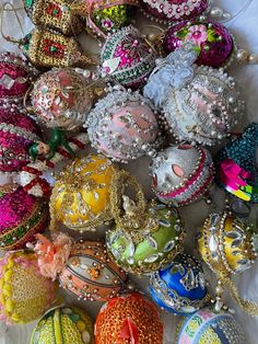 many different colored ornaments on a white table cloth with beads and chains hanging from them