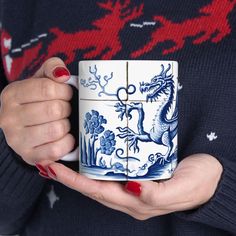 a woman holding a blue and white mug with dragon designs on the front, in her hands